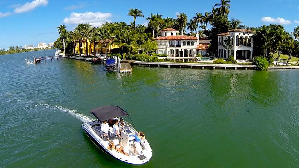 A white motorboat sailing past a luxurious home on the beach, MiamiCurated